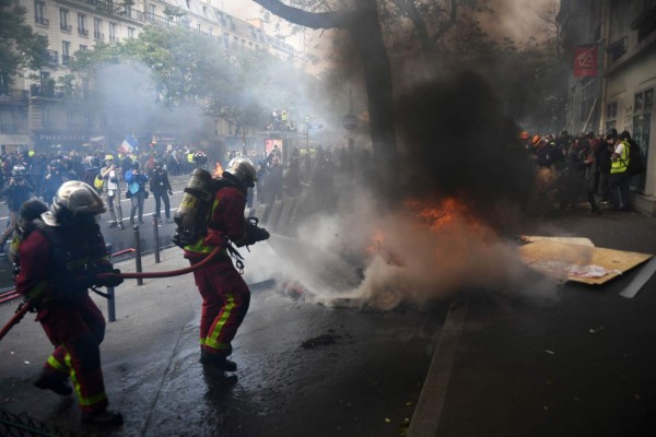 Firefighters extinguish a fire during clashes between police and demonstrators on the sidelines of the annual May Day rally in Paris on May 1, 2019. - Paris riot police fired teargas as they squared off against hardline demonstrators among tens of thousands of May Day protesters, who flooded the city on May 1 in a test for France's zero-tolerance policy on street violence. (Photo by Martin BUREAU / AFP)