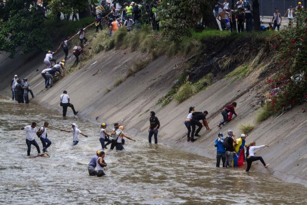 Demonstrators flee after riot police clash with protesters taking part in a rally against Venezuelan President Nicolas Maduro, in Caracas on April 19, 2017. Clashes broke out Wednesday at massive protests against Maduro, as riot police fired tear gas to push back stone-throwing demonstrators and a young protester was shot dead. Violence erupted when thousands of opposition protesters tried to march on central Caracas, a pro-government bastion where red-clad Maduro supporters were massing for a counter-demonstration. / AFP PHOTO / Leo Alvarez