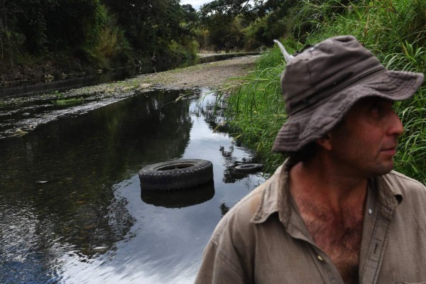 A man stands on a bank of the polluted Lempa river in the village of Piñuelas, 430km west of Tegucigalpa, on January 20, 2018.Thousands of fish have died in recent days due to contamination in the Lempa River caused largely by water that is used for washing coffee beans in processing plants that do not have a wastewater treatment system. The river has its sources in Guatemala where it is known as Olopa, then runs through Honduras and El Salvador as the Lempa. / AFP PHOTO / Marvin RECINOS