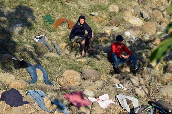 Central American migrants -heading in a caravan for the US- rest next to clothes put to dry on the bank of the Suichate River, where they spent the night, in Ciudad Hidalgo, Mexico, after crossing from Tecum Uman, Guatemala, on January 21, 2020. - Some 500 Central Americans, from the so-called '2020 Caravan', crossed Monday from Guatemala to Mexico, but over 400 were intercepted when National Guardsmen fired tear gas at them. (Photo by ALFREDO ESTRELLA / AFP)