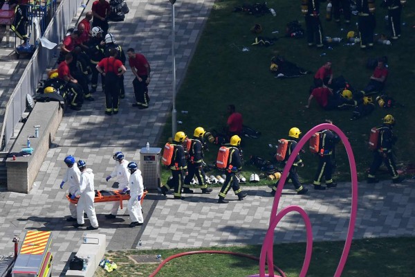 Firefighters carry the body of a victim on a stretcher (L) after a fire ripped through Grenfell Tower in west London on June 14, 2017.At least six people were killed Wednesday when a massive fire tore through a London apartment block overnight, with survivors voicing anger over longstanding safety fears at the 24-storey Grenfell Tower. / AFP PHOTO / Ben STANSALL