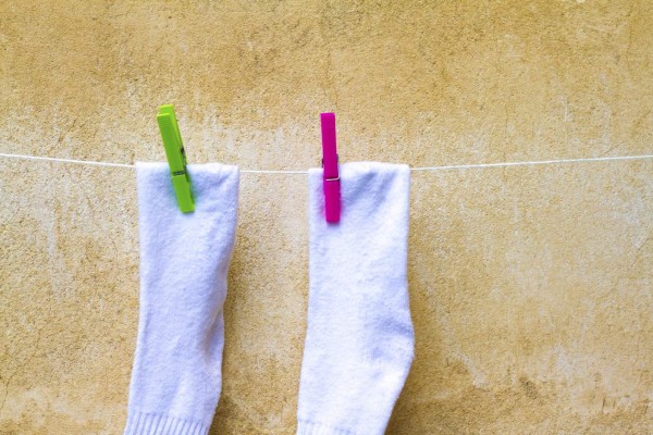 White Socks Drying on Line Against Old Yellow Wall, Italy. Pink and Green Clothespins. Copy space available.