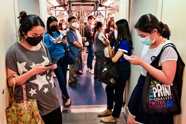 People wearing protective facemasks look at their phones as they stand in a city commuter train, in Bangkok, on February 1, 2020. - A Thai taxi driver has been diagnosed with the coronavirus, health officials said January 31, 2020 in the kingdom's first case of human-to-human transmission of the deadly SARS-like virus. Thailand now has detected 19 cases of the virus, the most declared outside of China. (Photo by Romeo GACAD / AFP)