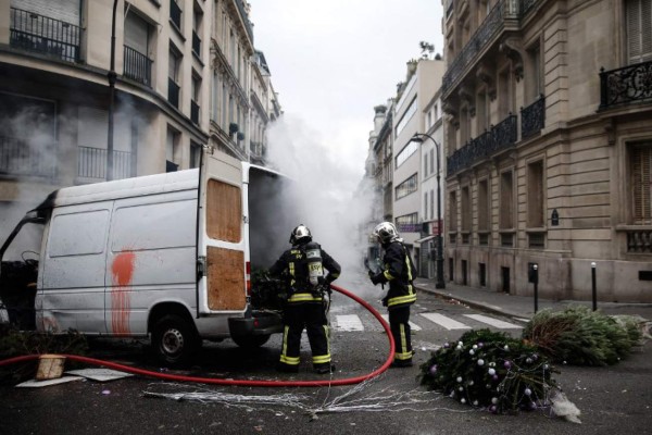 Firefighters stand next to a truck which was set on fire near the Champs Elysees avenue, on December 8, 2018 during a protest of 'yellow vests' (gilets jaunes) against rising costs of living they blame on high taxes in Paris. - Paris was on high alert on December 8 with major security measures in place ahead of fresh 'yellow vest' protests which authorities fear could turn violent for a second weekend in a row. (Photo by ABDUL ABEISSA / AFP)