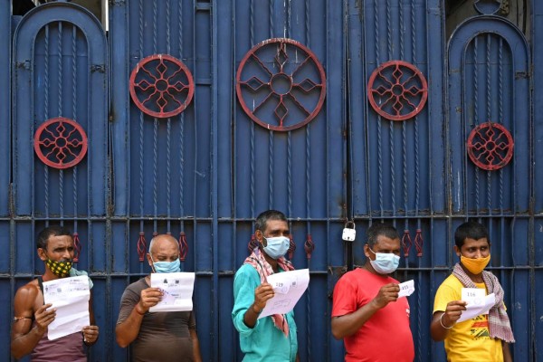 Workers hold documents as they wait for their turn to receive the first dose of Covishield vaccine against the Covid-19 coronavirus in a passenger bus converted into a mobile vaccination centre at a wholesale market in Kolkata on June 3, 2021. (Photo by Dibyangshu SARKAR / AFP)