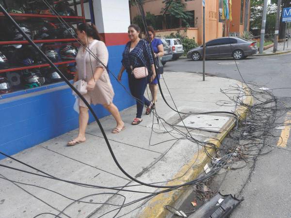Tres mujeres caminan por una acera de la tercera avenida, en la cual hay cables colgantes desde hace dos semanas.