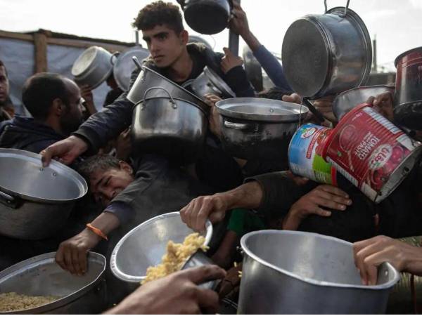 Un grupo de gazatíes claman por comida en un punto de repartición de alimentos.