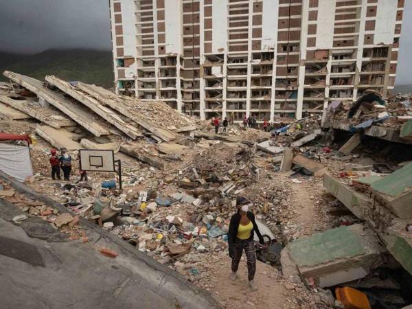 Fotografía de archivo que muestra a una mujer caminando entre los escombros de edificios colapsados por los terremotos del pasado 24 de junio, en La Guaira (Venezuela).