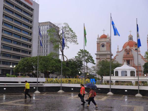 Dos hombres y una mujer caminan por el parque central de San Pedro Sula en una tarde lluviosa.