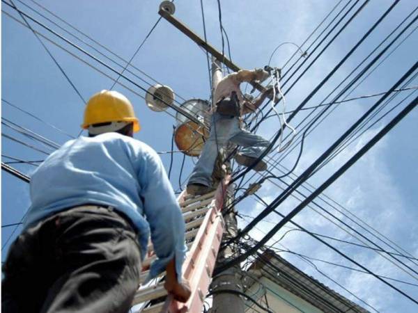 Dos técnicos realizan instalaciones eléctricas en postes del tendido público.