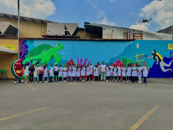 Colaboradores de Supermercados Colonial posando junto al mural finalizado; una obra de arte que refleja la conciencia y el compromiso medioambiental de la empresa.