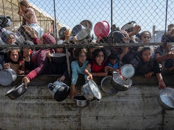 Niños y adultos se agolpan en una valla para recibir alimentos en la Franja de Gaza.