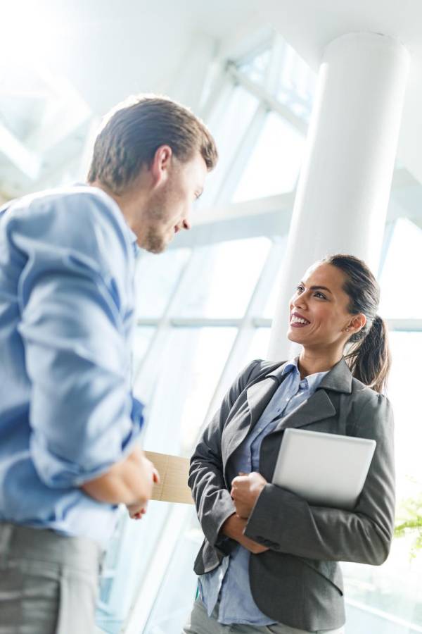 Happy female entrepreneur communicating with her male colleague while being in a hallway of an office building.