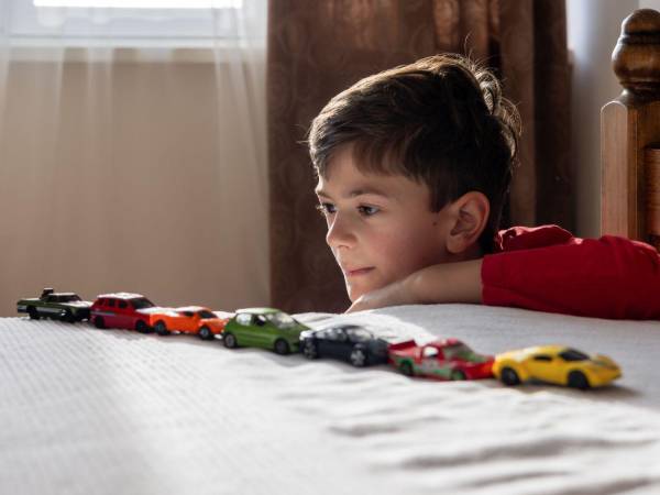 Un niño con una camisa roja alinea coches de juguete en su cama. signos de trastorno del espectro autista espectro autista (TEA) o de déficit de atención e hiperactividad (TDAH).