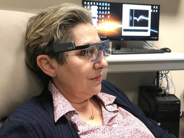Berna_Spikes: Imagen de una paciente ciega, con una gafas para el seguimiento de su mirada y el registro de su actividad cerebral en el fondo.