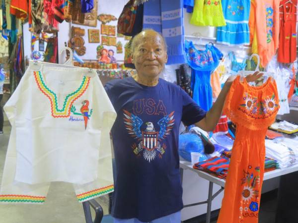 Mario Martínez, nacido en 1947, es uno de los comerciantes con mayor trayectoria en el Mercado Guamilito. En su puesto exhibe prendas típicas infantiles, vestidos bordados y accesorios con los colores de Honduras.