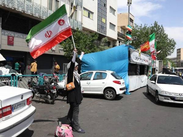Una mujer ondea una bandera de Irán en una calle de Teherán. Irán pide fin de sanciones y control estratégico en Ormuz.