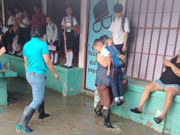 Una madre carga a su hijo en brazos debido al agua acumulada en el centro básico.