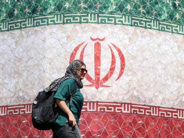 Una mujer iraní pasa junto a una valla publicitaria con la bandera nacional de Irán en la plaza Enqelab de Teherán, Irán. EFE/EPA/ABEDIN TAHERKENAREH.
