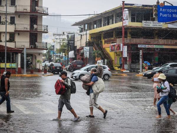 Personas caminan por una calle encharcada debido a las fuertes lluvias en el balneario de Acapulco, estado de Guerrero (México).