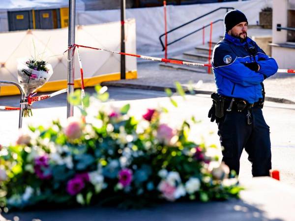 Un policía monta guardia junto a flores depositadas cerca del lugar del incendio declarado en el bar-lounge Le Constellation, este jueves en Crans-Montana, Suiza.