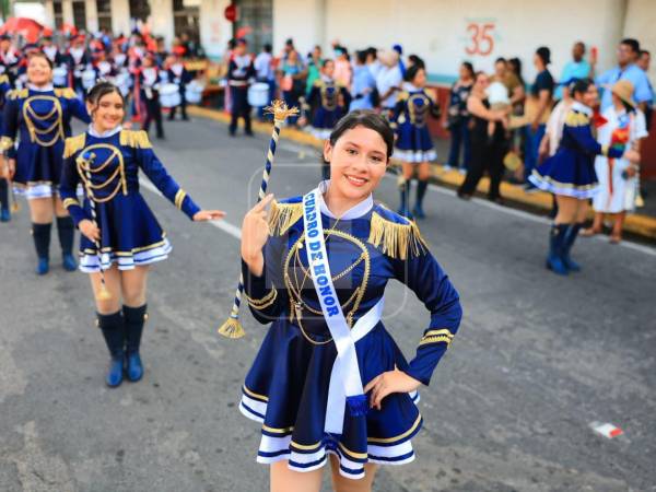 Una estudiante del Cuadro de Honor luce sonriente con su bastón de mando y banda distintiva, encabezando las palillonas y banda de su centro educativo.