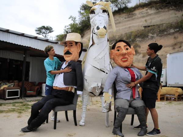 Dos jóvenes preparan monigotes, conocidos como ‘Año Viejo’, que representan a la presidenta de Honduras, Xiomara Castro, y al expresidente Honduras, Manuel Zelaya, este domingo en la aldea de Germania, al sur de Tegucigalpa (Honduras).