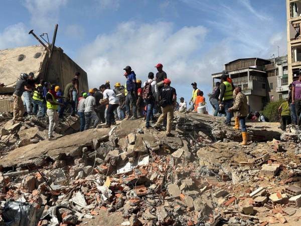 Personas caminan sobre escombros de edificios derrumbados por los terremotos este jueves, en el sector San Bernardino, en Caracas (Venezuela).