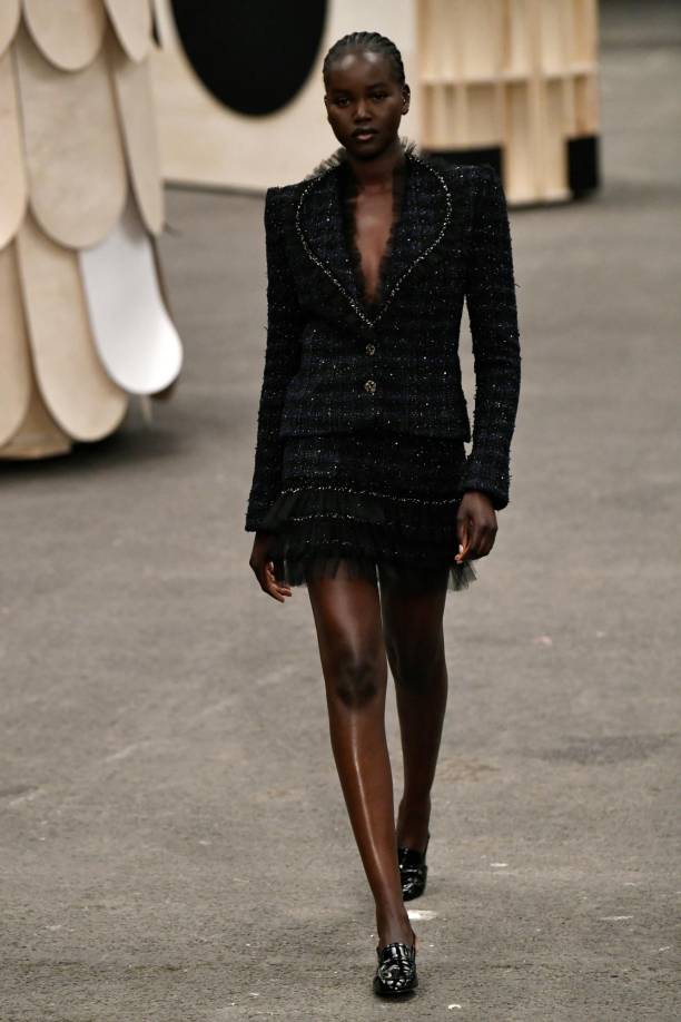 Bajo una chaqueta con mangas abullonadas y marcada en la cintura, sobresale una falda de organza blanca, como si fuera lencería, mientras que en el cuello una pajarita negra destaca como si fuera una joya.