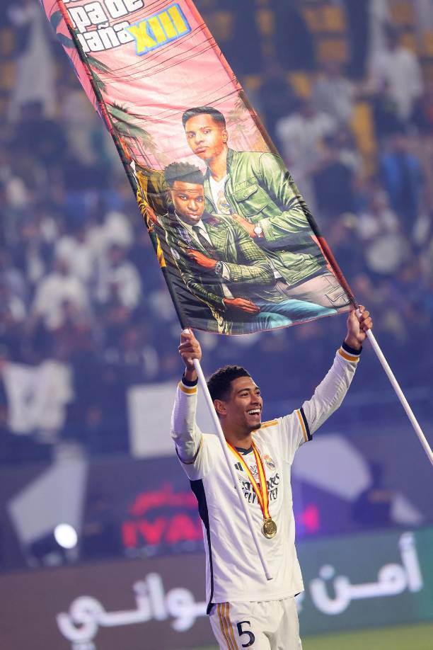 Jude Bellingham levantando una pancarta en la que aparece él junto a Vinicius y Rodrygo.