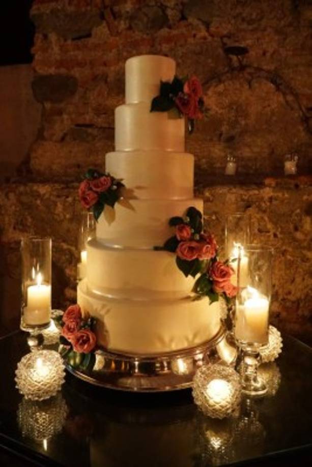 El pastel de seis niveles fue sutilmente adornado con rosas lila y velas que iluminaban el rincón amurallado.<br/>