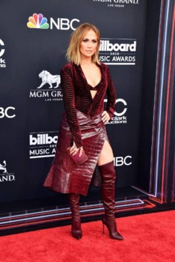 Jennifer López luce espectacular con un traje estilo abrigo que deja al descubierto un pronunciado escote y unas botas altas.