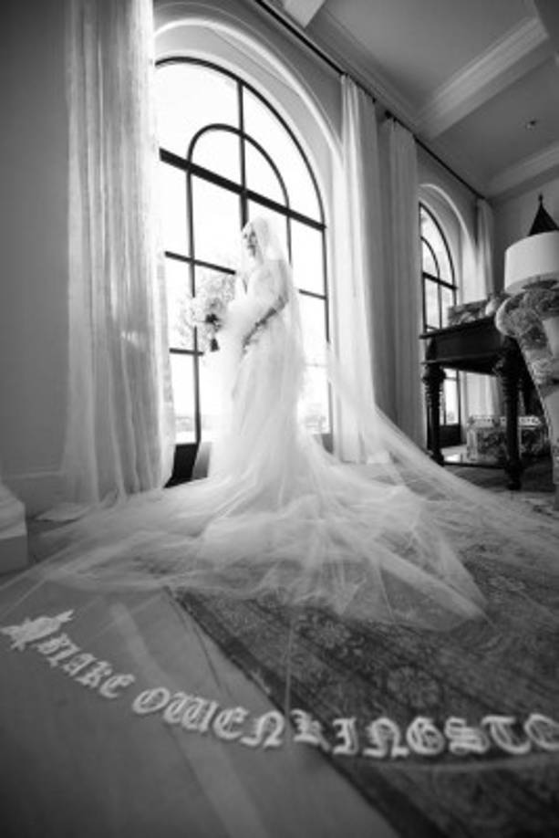 Gwen Stefani wore custom Vera Wang Haute for her wedding to Blake Shelton.<br/> <br/>She chose a custom lily white silk georgette and hand tumbled tulle high low gown with a plunging neckline and a cut away back. The gown was worn with a lily white chapel length veil featuring hand embroidered names of Blake, Gwen, Kingston, Zuma and Apollo flanked by 2 white roses at the hem of the veil.<br/> <br/>For the reception she chose a custom lily white Italian silk crepe and hand tumbled tulle strapless mini dress with hand pieced silk, crystal and sequin embroidered foliage delicately trickling from the waist down the skirt. The embroidery is highlighted by a pair of hand sewn love birds symbolizing the couple. The are joined by 3 baby love birds representing Gwen's children. <br/><br/>Photos courtesy of Jeremy Bustos