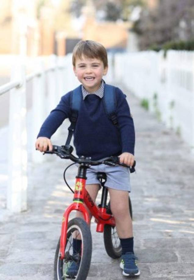 La foto muestra a Louis sonriendo de oreja a oreja en una bicicleta roja en el Palacio de Kensington el pasado miércoles, poco antes de su primer día de preescolar en Willcocks Nursery School de Londres. Louis aparece con su uniforme escolar, un suéter azul con cuello a rayas y pantalones cortos azules.La adorable foto fue tomada por su duquesa Kate, una ávida fotógrafa.