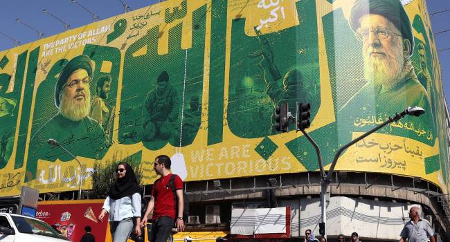 Iraníes transitan ante una valla publicitaria en Teherán que representa al exlíder de Hizbulá, Hasán Nasrala (i) y al difunto líder supremo iraní, Alí Jameneí (d). EFE/EPA/ABEDIN