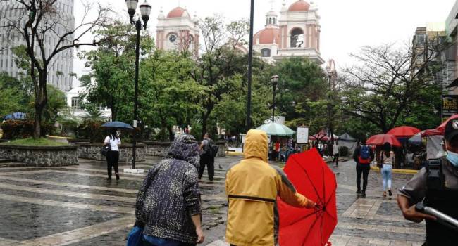 Hondureños se cubren de la lluvia en San Pedro Sula.