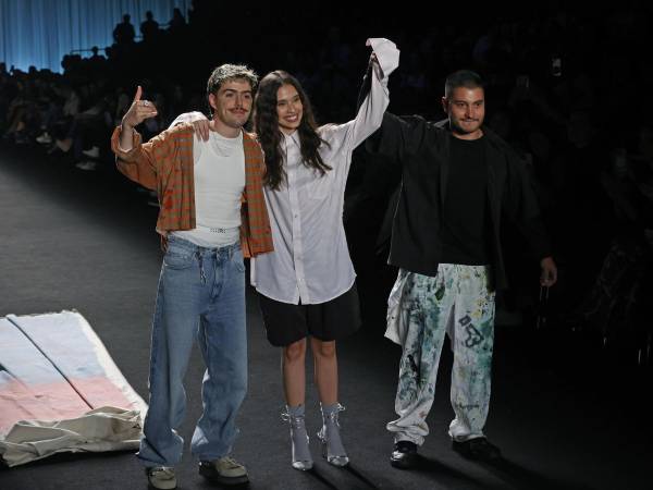 El baterista de la banda colombiana Morat, Martín Vargas (i), saluda al público presente al lado de dos de sus modelos luego de presentar prendas de la marca 'General' en una pasarela del Bogotá Fashion Week.