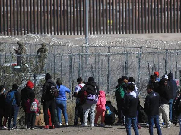 Un grupo de migrantes frente al muro en la frontera de EEUU y México.