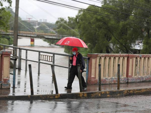 Un ciudadano camina mientras al fondo se ve el elevado nivel del río Choluteca, en Tegucigalpa (Honduras), en una fotografía de archivo.