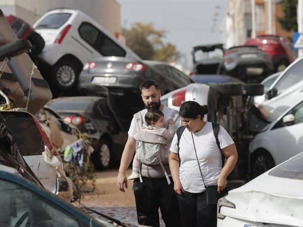 Una pareja con su bebé camina entre una montaña de coches hacinados tras las inundaciones sufridas en la localidad valenciana de Paiporta.