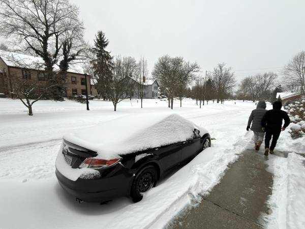 Dos personas caminan al lado de una calle afectada por la nieve este domingo en la ciudad de Hudson, Ohio (EE.UU.).