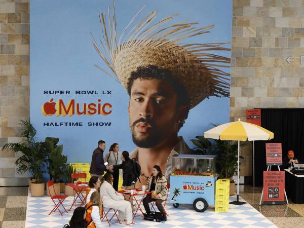Gente sentada junto a un cartel del cantante Bad Bunny, protagonista del espectáculo del medio tiempo del Super Bowl, que se disputa este domingo.