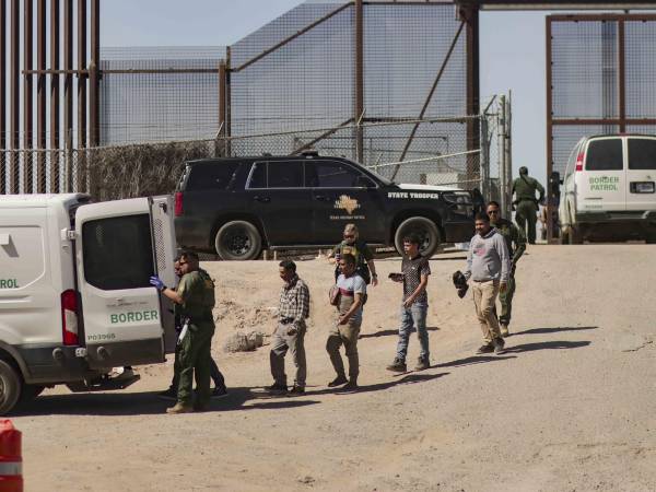 Migrantes detenidos son llevados por miembros de la Patrulla Fronteriza estadounidense a un vehículo, junto al muro fronterizo en El Paso, Texas (EE.UU).