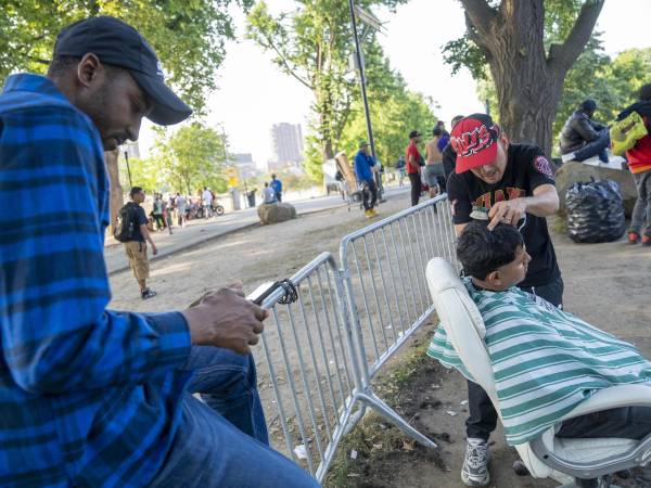 Fotografía que muestra un inmigrante mientras le corta el cabello a otro afuera del refugio de Randall Island en Nueva York.