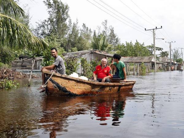 Tres hombres navegan en un bote para ofrecer ayuda ante las intensas lluvias y algunas penetraciones del mar en zonas costeras bajas en el occidente de Cuba tras el paso del huracán Helene al oeste de la isla.