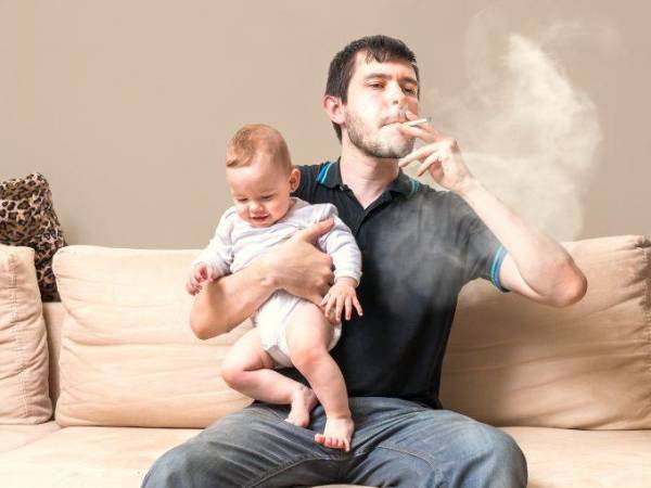 Foto de ilustración, padre fumando con su hijo en brazos. Situación que no debe ser permitida.