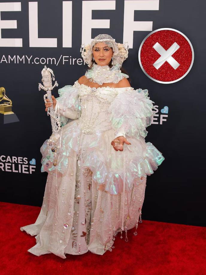 El look de Ferrell llamó la atención. <b>Llevó un vestido voluminoso de estilo barroco o victoriano, predominando el color blanco</b>. La prenda estuvo adornada con múltiples detalles decorativos, como encajes, transparencias, perlas y aplicaciones brillantes que refuerzan su<b> carácter teatral. </b>La parte superior incluyó un diseño de cuello alto y hombros descubiertos, con una estructura elaborada. El estilismo se complementó con un cetro decorativo que refuerza una estética de reina o figura de fantasía, y un toque llamativo que aporta simetría y completa la temática del atuendo.