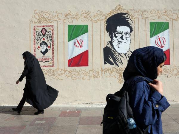 Mujeres iraníes caminan junto a un mural del difunto Líder Supremo iraní, el ayatolá Ali Jamenei, en una calle de Teherán,