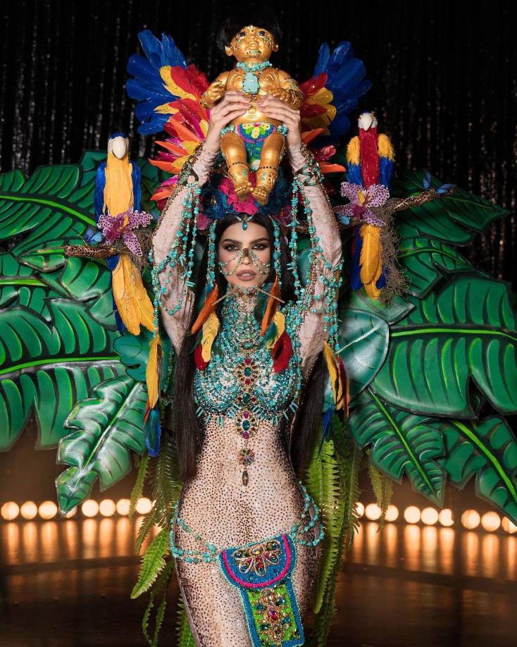 Recientemente, Ileana reveló las imágenes del traje típico que usará en el Miss Universo, inspirado en el personaje ficticio de Yamira “La reina madre de la paz”. A través de sus redes sociales la criolla detalló que esta fantasía evoca el estado Amazonas que representó en el Miss Venezuela, diseñado por Carlos Pérez.La pieza de malla cuenta con más de 20 mil cristales bordados, incrustaciones en oro y plumas multicolores que adornan el penacho ornamenado con guacamayas.Fuente: Hola! y AS USA Latino