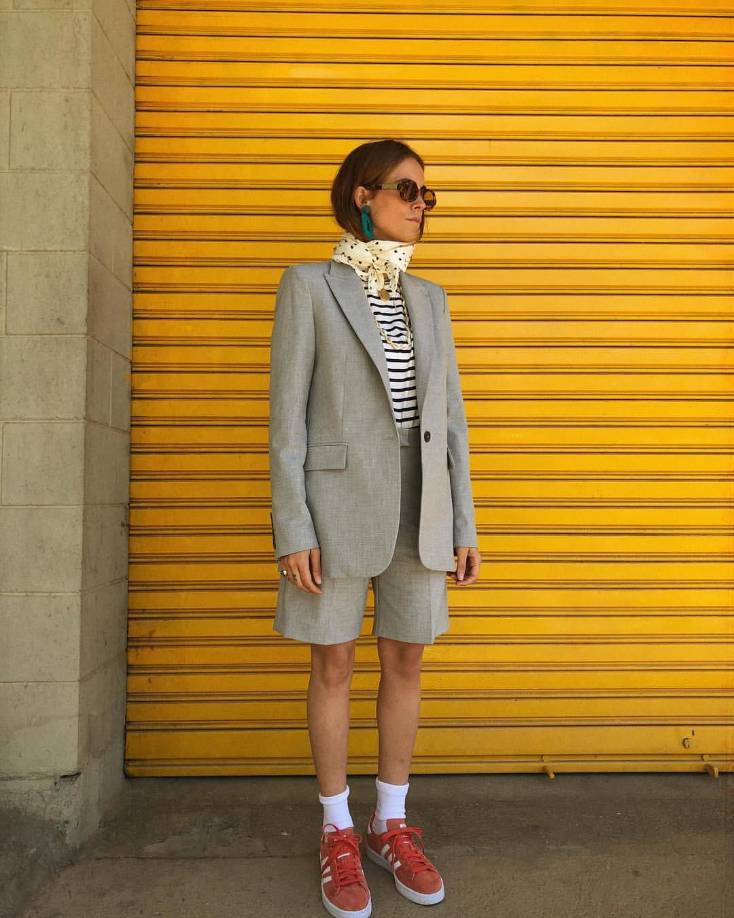 Otro combinación en tendencia son los trajes con bermudas. Si mezclas la camisa con uno en tono neutro como este en gris y complementas con accesorios como pañuelo y tenis coloridos, habrás creado un look moderno para ir a la oficina.